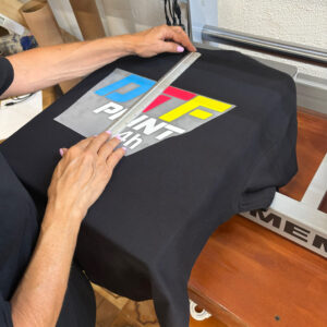 Una persona posiziona con precisione un transfer DTF colorato su una maglietta nera, utilizzando un righello per allineare la grafica prima della stampa.